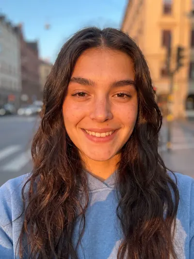 Golden-hour street selfie: long wavy hair, a big smile.