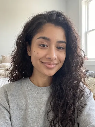 Selfie: long curly hair, a nose stud, a few dark marks on one cheek.